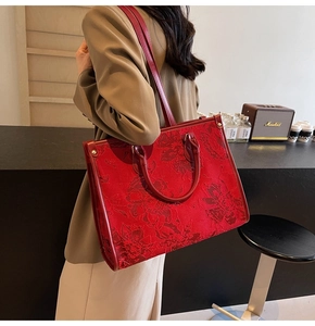 Detail of red floral jacquard tote bag with leather straps on a modern background