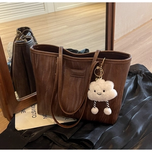 Détail d'un sac cabas marron à texture ondulée avec un charm en peluche nuage blanc