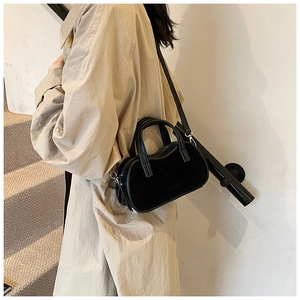 Detail of a minimalist black leather Boston bag with silver hardware on a trench coat
