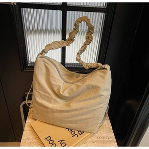 Detail of beige nylon tote bag featuring a textured pleated shoulder strap and zipper