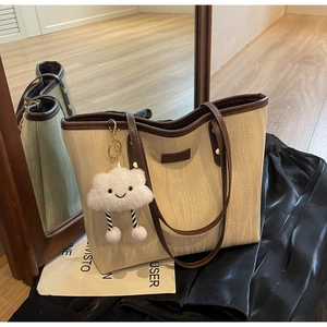 Détail du sac cabas beige à texture ondulée avec anses brunes et breloque nuage doux
