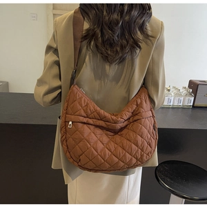 Gros plan d'un sac bandoulière matelassé marron foncé montrant sa structure demi-lune