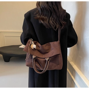 Dettaglio borsa tote in pelle scamosciata marrone scuro con ciondolo guanto da baseball e tracolla