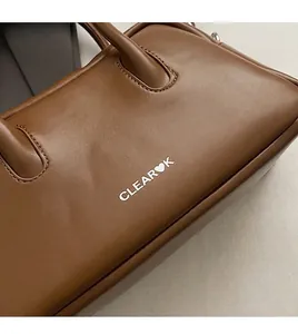 Detalle de textura de cuero marrón y logo blanco en bolso vintage tipo almohada