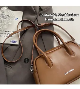 Detalle de un bolso bowling de cuero marrón con asas redondas y correa ajustable