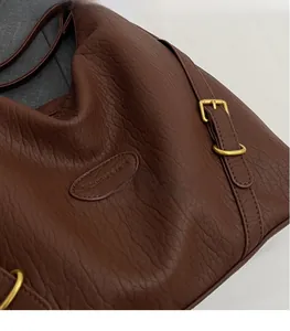 Close-up of brown pebbled leather texture and gold buckle detail on a versatile handbag