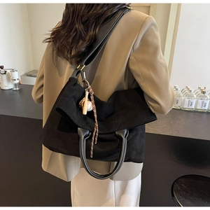 Dettaglio di una grande borsa tote nera con ciondolo da baseball e tracolla su un modello