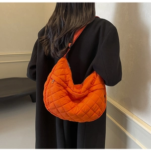 Détail d'un sac bandoulière orange matelassé porté sur un manteau d'hiver noir