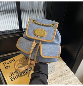 Détail d'un sac à dos en denim avec tissu bleu clair, bordures en cuir brun et chaîne en métal