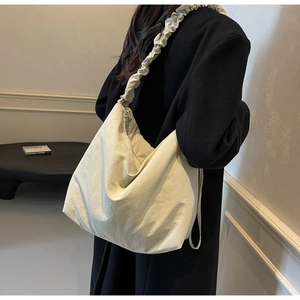 Detail of a beige cloud pleated strap crossbody bag shown from a back side view on a model