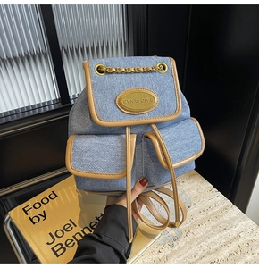Détail d'un sac à dos en jean bleu avec garniture en cuir marron et chaîne dorée