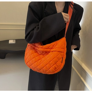 Gros plan du sac matelassé orange vif avec large bandoulière sur blazer noir