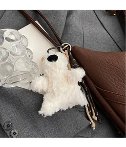 Plush white bear charm with braided lanyard attached to a brown leather crossbody bag