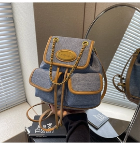 Détail du sac à dos en denim bleu avec garniture en cuir brun et chaîne dorée