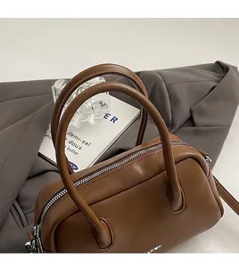 Detalle de bolso de cuero marrón con asas redondas y cremallera de metal plateado