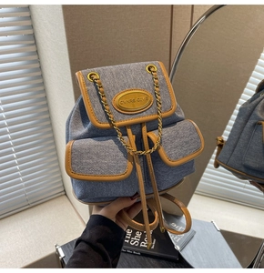 Détail d'un sac à dos en denim bleu avec bordure en cuir marron et plaque logo dorée