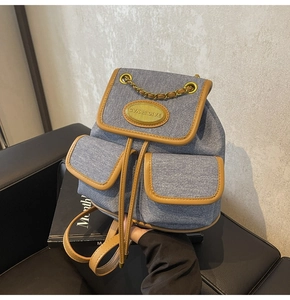 Détail d'un sac à dos en jean bleu avec garniture en cuir brun et chaîne dorée chic