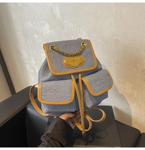 Détail du sac à dos en denim bleu avec bordure en cuir marron et chaîne dorée décorative
