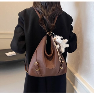 Brown leather hobo bag with gold buckle and plush bear pendant shown on model's shoulder