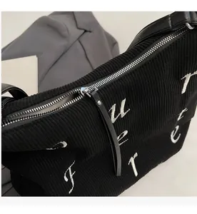 Detail of smooth metal zipper and white embroidery on black corduroy tote bag
