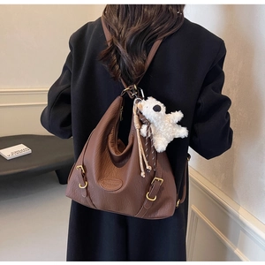 Detail of brown lychee texture backpack featuring a plush bear charm and metallic hardware