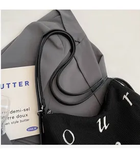 Detail of black corduroy shoulder bag showing strap attachment and letter embroidery