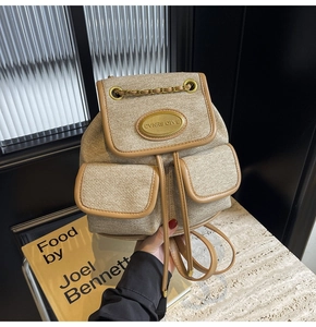 Gros plan du sac à dos en tissu beige avec garniture en cuir brun et plaque dorée