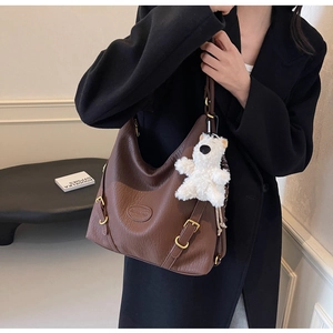 Detail of brown leather tote bag with gold buckle and white teddy bear charm