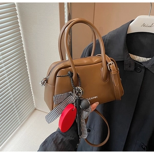 Detalle de bolso Boston de cuero marrón con colgantes decorativos y acabados metálicos