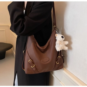 Close-up of brown textured leather shoulder bag featuring a cute white teddy bear charm