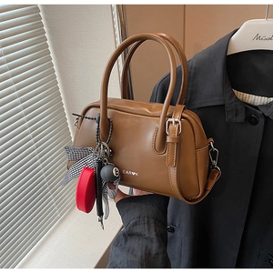 Detalle de un bolso tipo Boston en cuero sintético marrón con colgantes decorativos y lazo