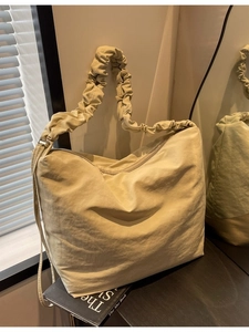 Minimalist beige tote bag with pleated wide shoulder strap shown in a sunlit interior