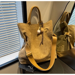 Dettaglio della borsa tote in pelle scamosciata senape con ciondolo da baseball e tracolla