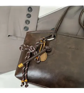 Detail of dark brown leather tote with woven rope strap and tennis racket charm