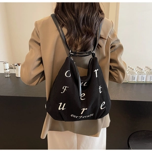 Detail of black corduroy tote bag with white lettering worn as a crossbody backpack