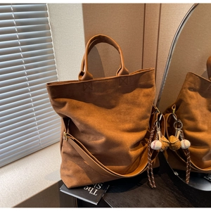 Dettaglio di una borsa tote in pelle scamosciata marrone con ciondolo da baseball sportivo
