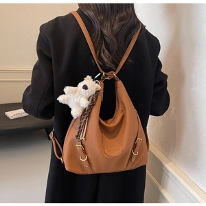 Detail view of the brown leather hobo bag with a plush bear charm and side metal buckle