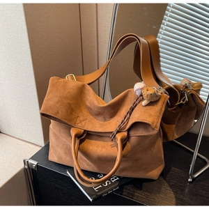Dettaglio di una borsa tote in pelle scamosciata marrone con manici in pelle e charm