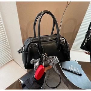 Detalle de bolso bandolera negro de piel con lazo de cuadros y colgantes decorativos
