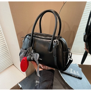 Detalle de un bolso Boston negro con textura de cuero, lazo de cuadros y colgantes