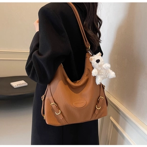 Detail of caramel brown litchi grain leather hobo bag with a cute plush bear charm
