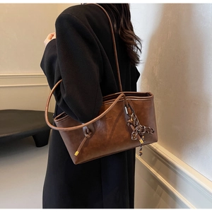 Detail of a brown leather tote bag featuring a knotted strap and decorative polka dot tassel