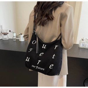 Detailed view of black corduroy tote bag showing embroidered lettering on a model