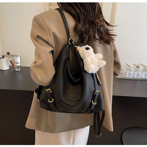 Detailed view of black pebbled leather backpack with gold buckles and plush bear charm
