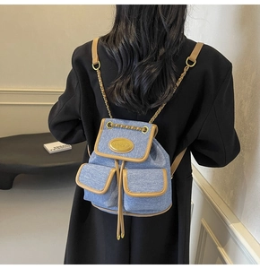 Détail du sac à dos en jean bleu clair avec garniture en cuir brun et chaînes dorées
