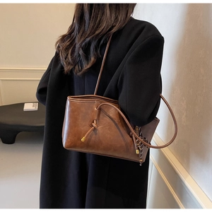 Detail of caramel brown leather tote bag with knot decor and woven charm on shoulder