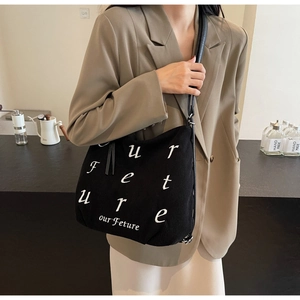 Detail of black corduroy tote bag featuring white embroidered 'Our Future' artistic text