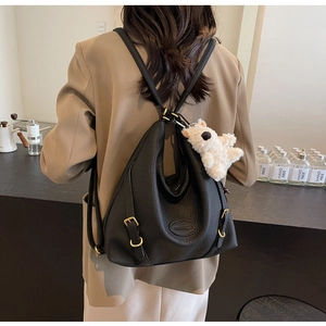 Close-up of black lychee leather backpack with golden hardware and white plush bear charm