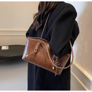 Detail view of vintage brown leather tote bag with woven charm on black coat