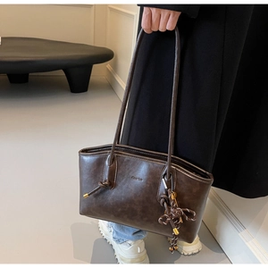 Detail of dark brown tote bag in matte leather featuring a stylish woven knot accessory